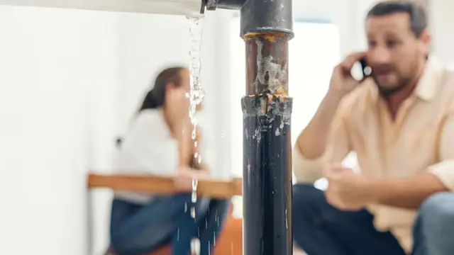 Homeowners on the phone beside a leaking pipe