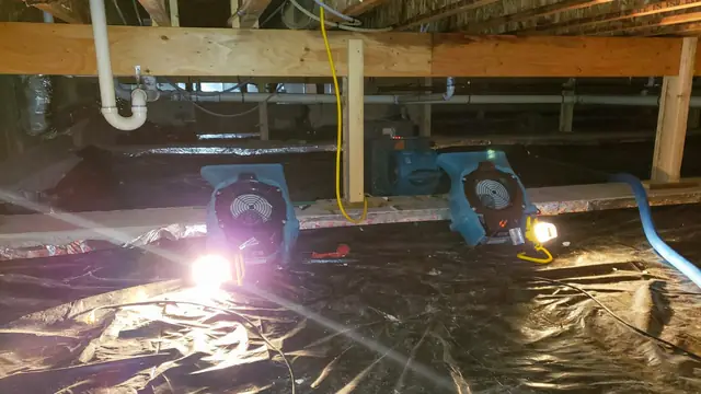 Crawl space with drying fans and plastic sheeting under the floor framing