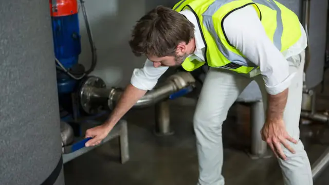 Worker in a safety vest checking the pipes at a water heater
